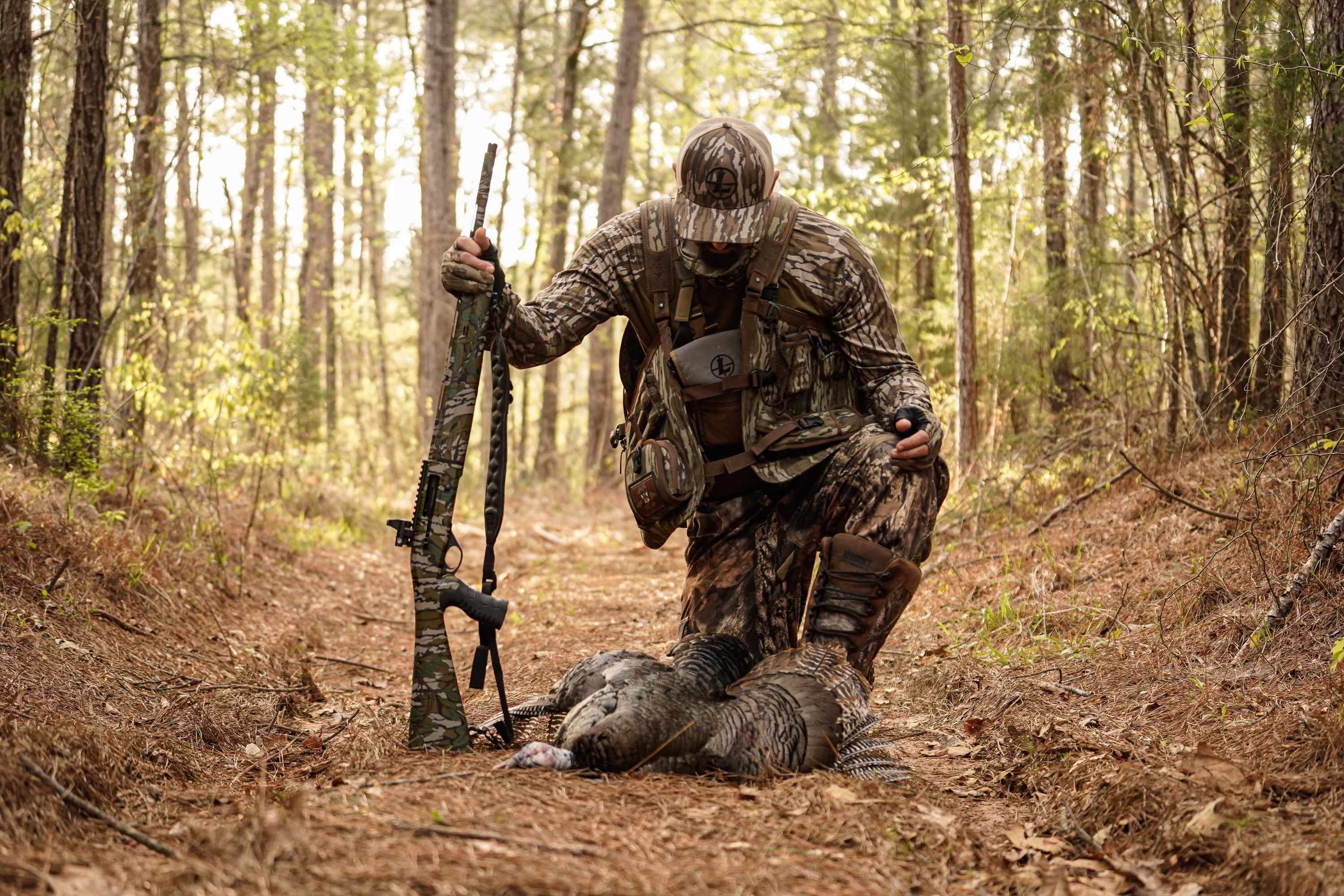 male hunter kneels down with his turkey and rifle in hand