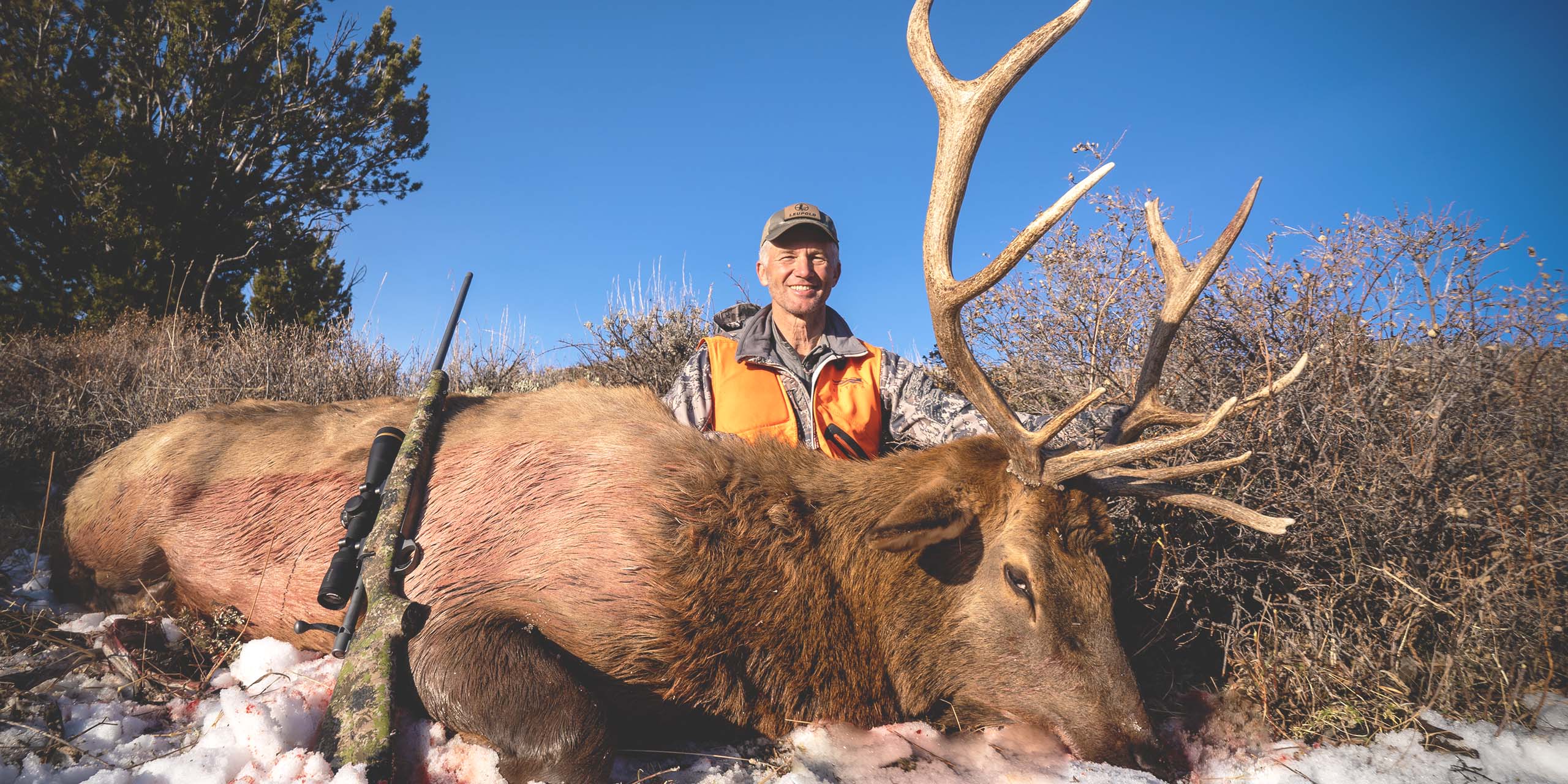 Hunter Randy Newberg sits with his trophy kill of an Elk in a field.