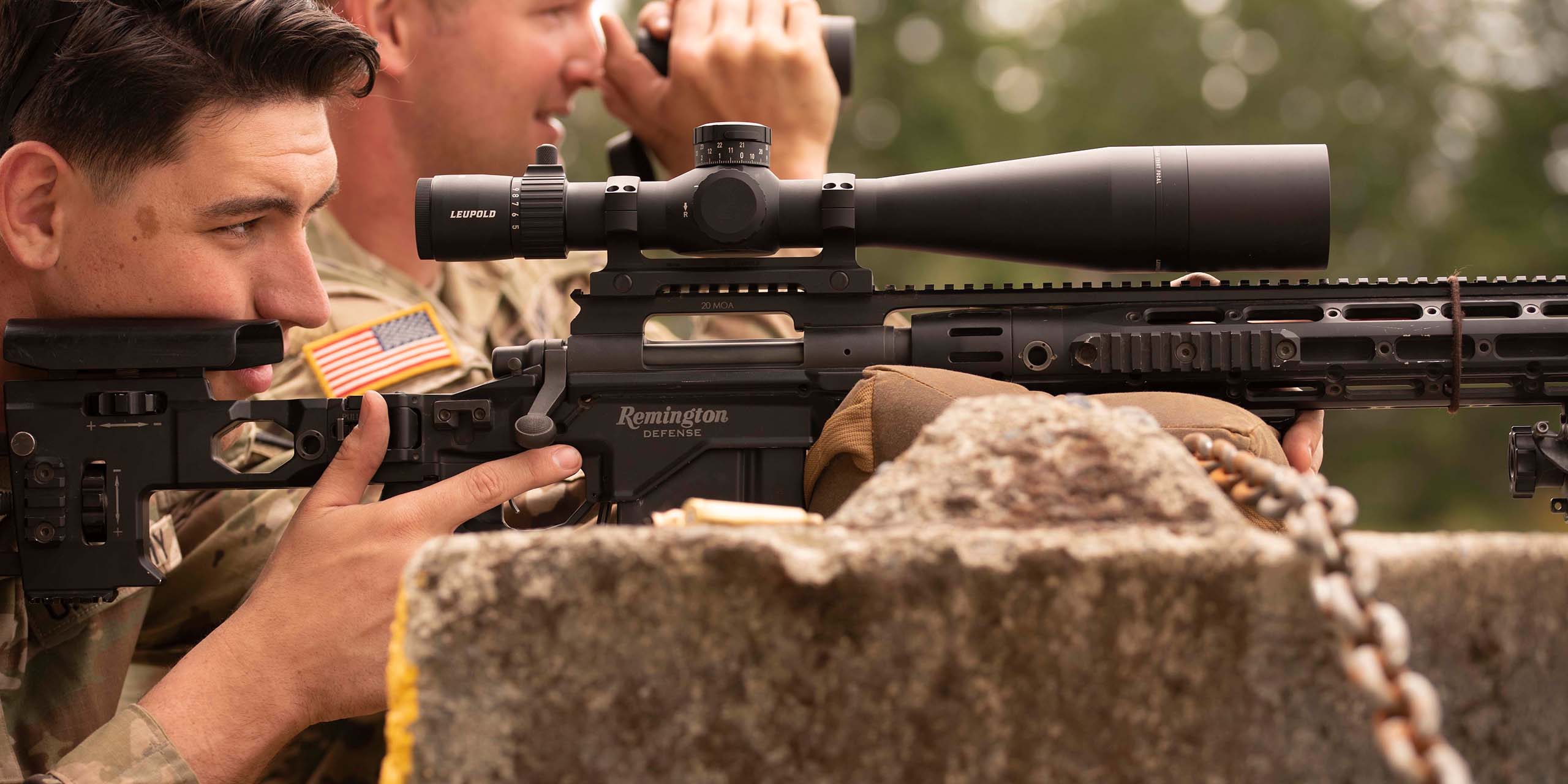 Profile image of a rifleman and a spotter looking down range. The rifleman is looking through a Mark 5HD riflescope.