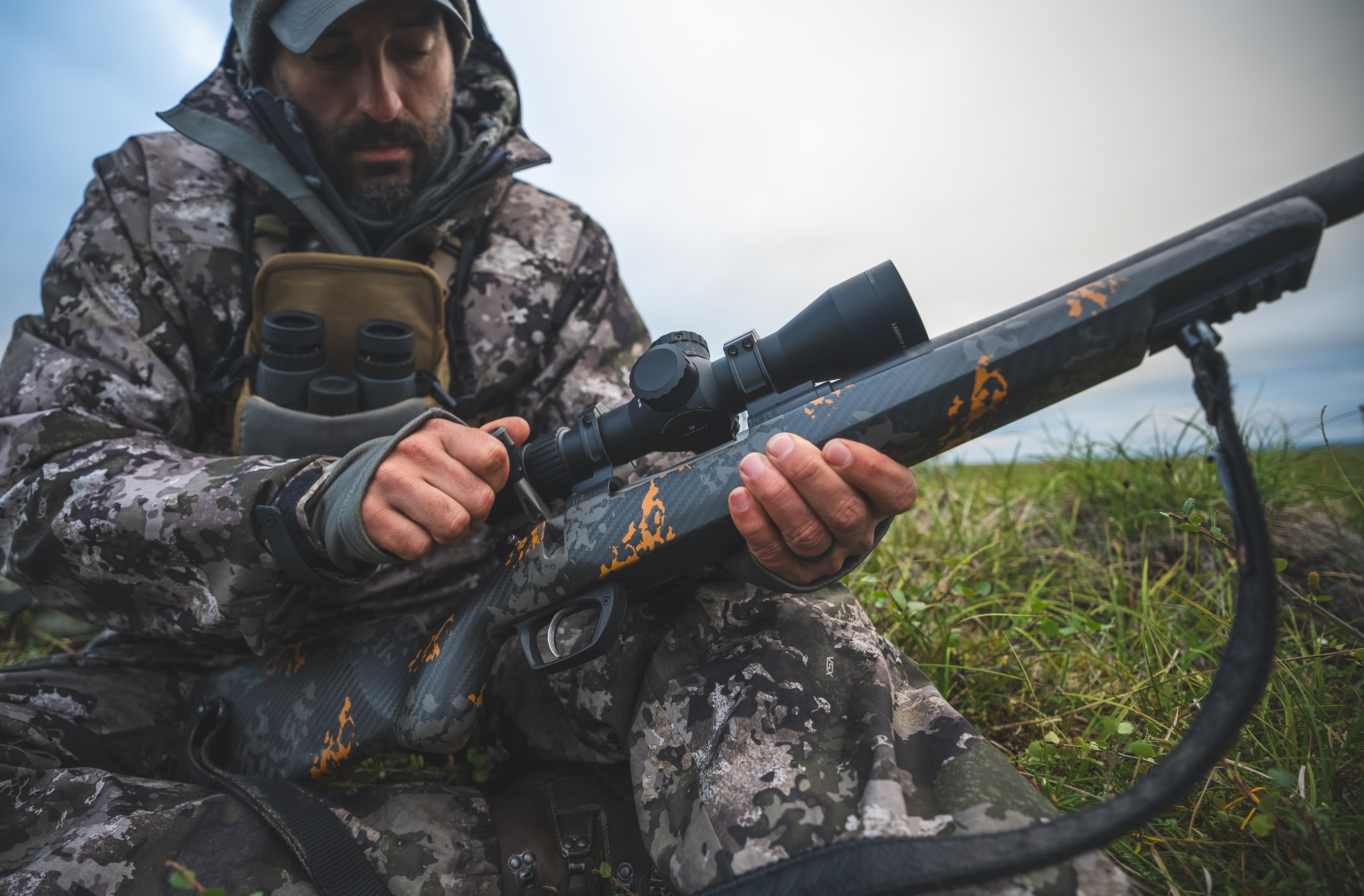 Male shooter holding a rifle topped with a Leupold Mark 5HD riflescope in a field