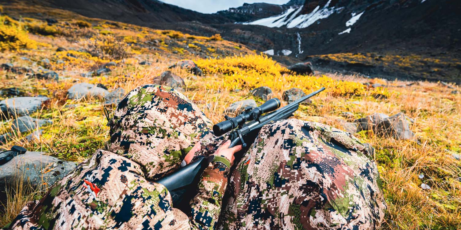 female hunter lays on tundra with rifle on backpack