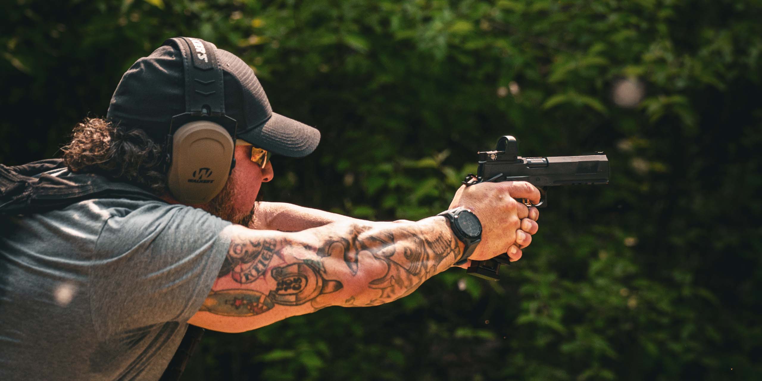 Male shooter in shooting gear holding a custom handgun with a Leupold DeltaPoint Pro red dot sight mounted in top of the firearm.