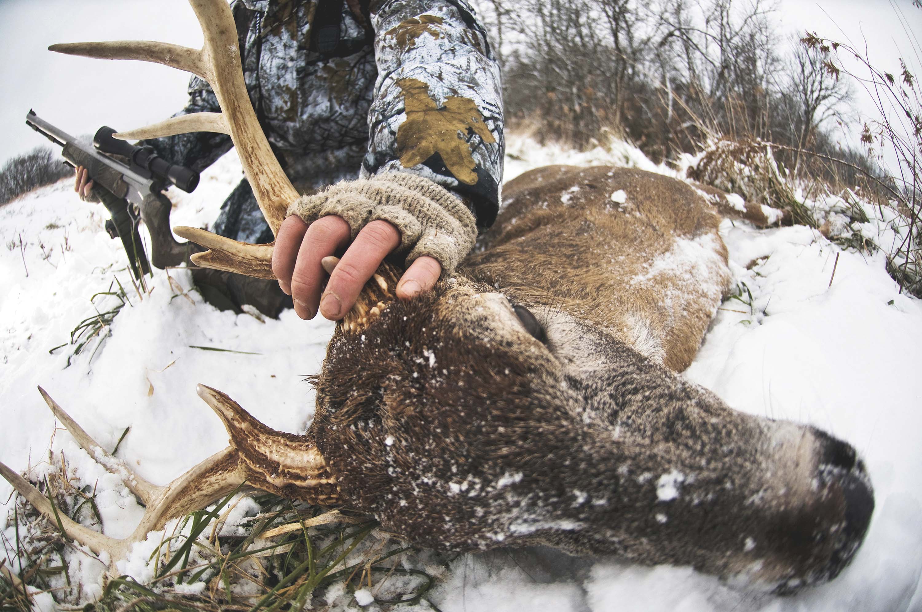 Hunter holding deer antlers in snow with rifle and Leupold riflescope.