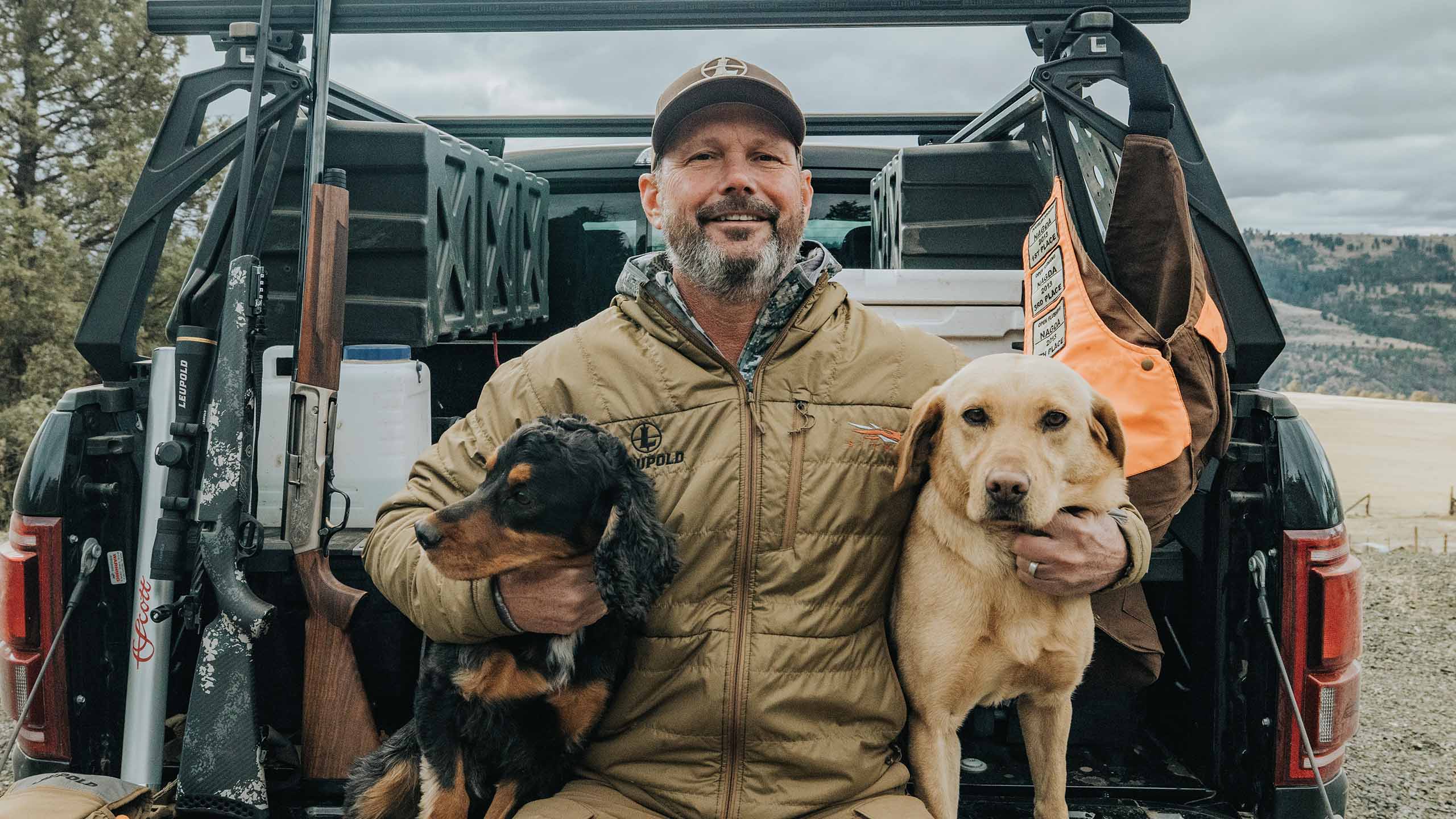 Bruce Petter, CEO of Leupold & Stevens, sitting on the edge of his truck bed with his two hunting dogs.