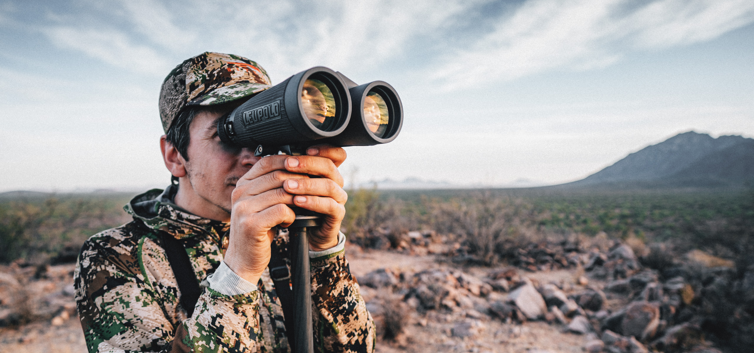 hunter wearing camouflage and hat glassing with leupold binoculars