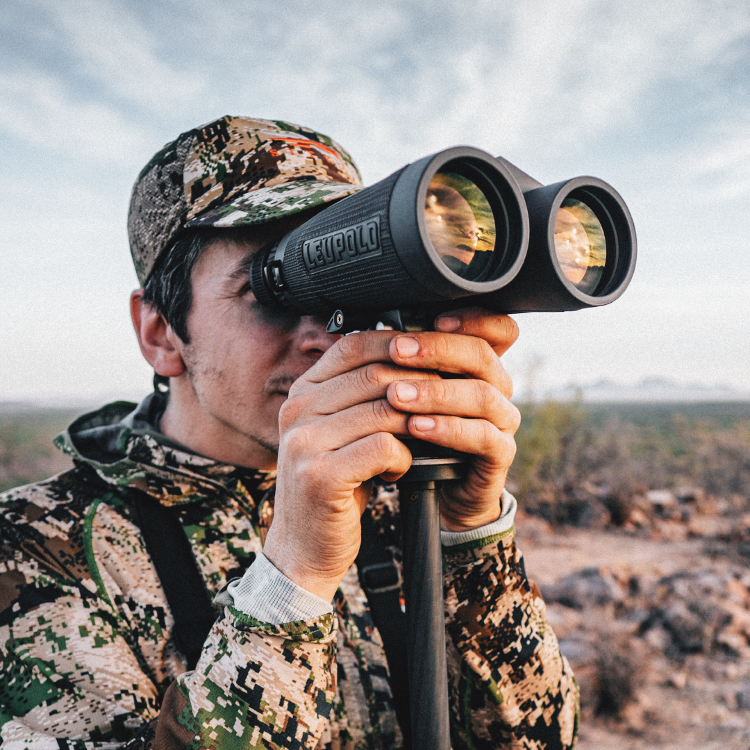 hunter wearing camouflage and hat glassing with leupold binoculars