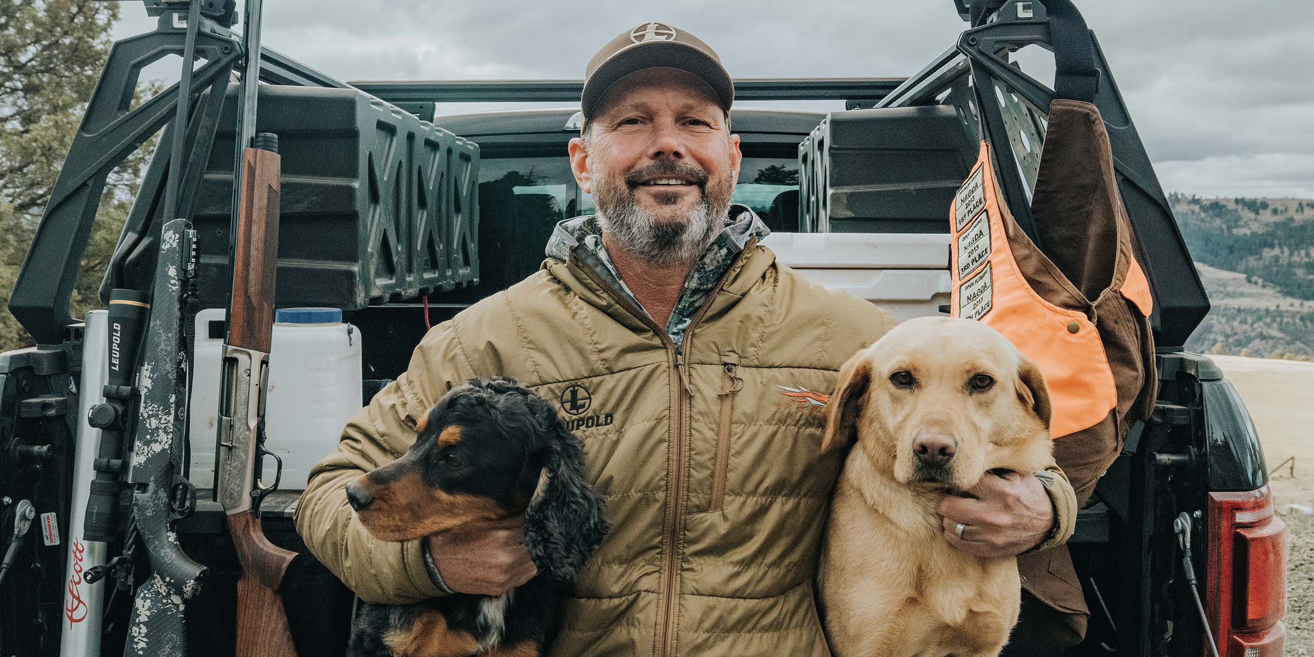 Bruce Pettet, CEO of Leupold & Stevens, sitting on the edge of a truckbed with his two dogs.